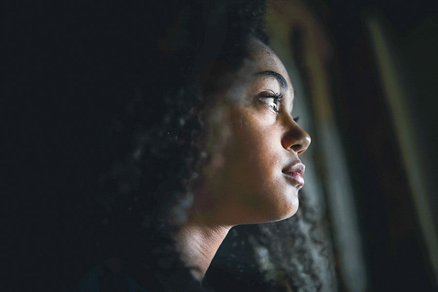 close-up of teen girl looking out window, reflecting with a sad expression