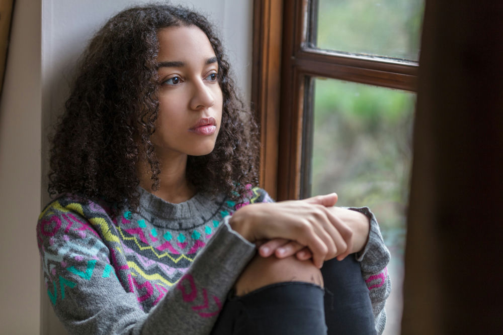 teen girl staring out windowsill, showing signs of behavioral struggles