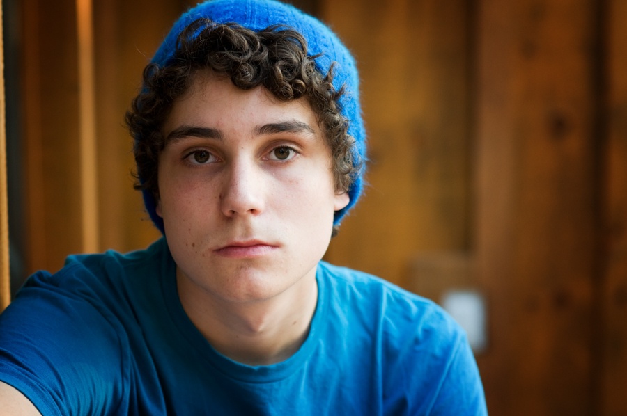 Teen boy in blue shirt and beanie staring with a somber, distant look
